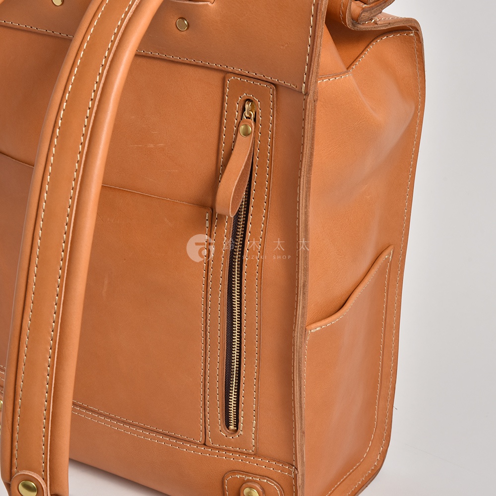 職人手作皮革後背包，淺棕色，有拉鍊口袋與側袋，縫線精緻。