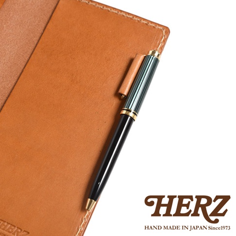 職人手作皮革輕便記事本書套，淺棕色皮革，附一支黑色筆桿、綠色條紋筆夾和金色筆頭的鋼筆，鋼筆固定在書套側邊。