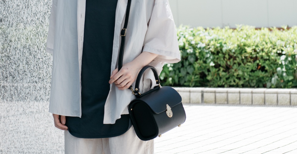 黑色皮革復古杜勒斯手提包，配有金色金屬鎖扣和可調節肩帶。