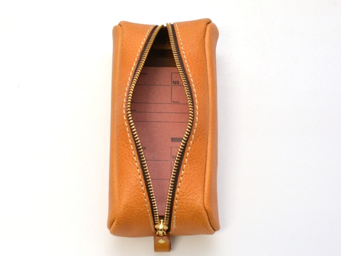 咖啡色皮革圓角收納筆袋，拉鍊開啟，內有紅色紙張，白色縫線裝飾。