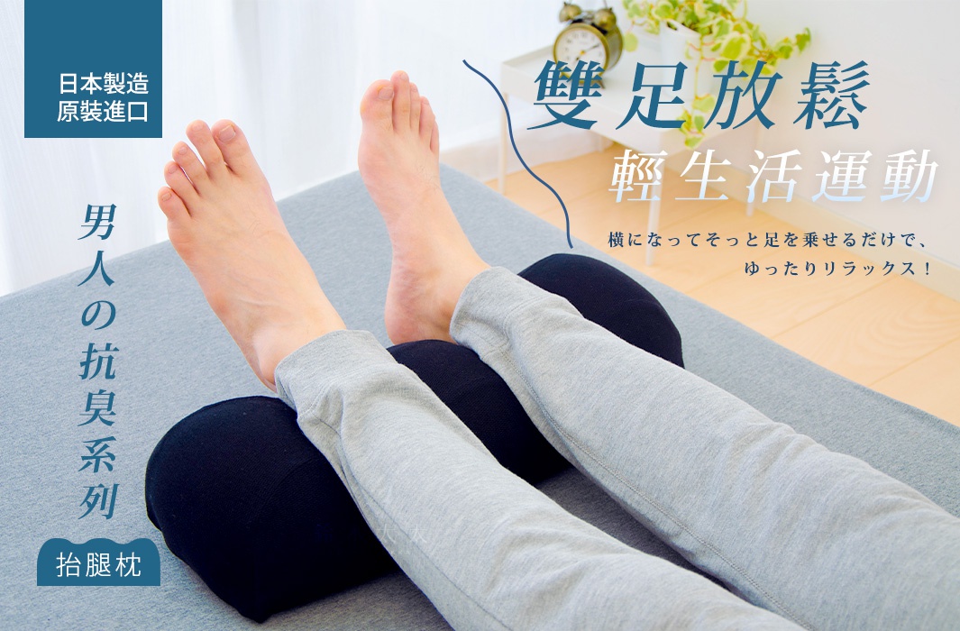 一雙黑色的圓筒形抬腿枕，上面放著一雙穿著灰色長褲的男性雙腿，雙腳裸露在外，枕頭置於膝蓋下方，整體畫面呈現居家放鬆的氛圍。