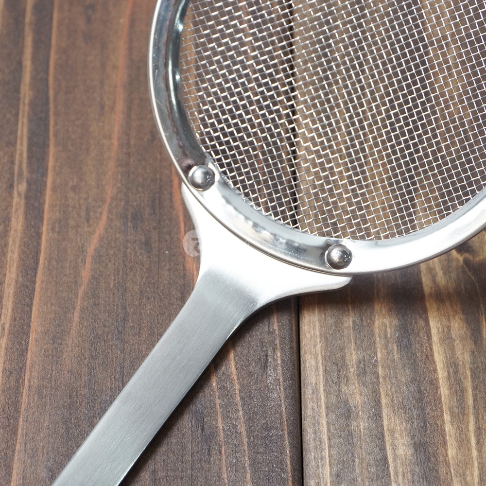 不鏽鋼撈油勺，具有細密的網篩和金屬手柄，整體呈現銀色光澤，置於木紋背景上。