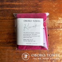一條包裝好的深紅色細纖毛巾，毛巾材質柔軟，帶有摩登復古風格的標籤，標籤上印有「OBORO TOWEL Kiwami」字樣，以及「The skills of master craftsmen, perfected over 100 years. Astonishingly voluminous and addictively soft.」等英文說明。