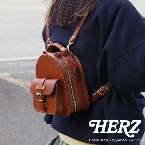職人手作皮革迷你後背包，採用棕色皮革，設有前置翻蓋口袋、拉鍊開合及可調節肩帶，展現精緻工藝。