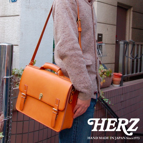 職人手作皮革經典三扣兩用商務公事包，亮橘色皮革，配有頂部提把、可拆卸肩帶、雙皮帶釦和金色轉鎖，風格復古。