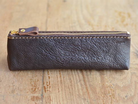 職人手作Organ三角收納筆袋，深棕色皮革材質，設有金色拉鍊與同色系皮革拉環，車縫線明顯，表面有自然皮革紋理，品牌Logo印於右側。