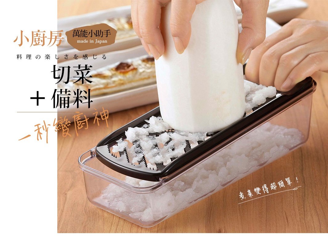 圖片文字：小廚房萬能小助手 made in Japan 料理の楽しさを感じる 切菜＋備料 一秒變廚神 煮菜變得超簡單 一名使用者正雙手持握一根白蘿蔔，在黑色的刨絲器上進行研磨，刨出的蘿蔔泥直接掉落並收集在下方透明的長方形儲存盒中，背景桌面上還擺放著一盤烤魚料理。