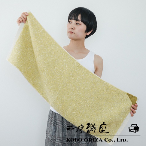 一位女性手持一條淺黃色和白色相間的棉麻混紡毛巾，毛巾表面帶有紋理，邊緣有白色織邊。