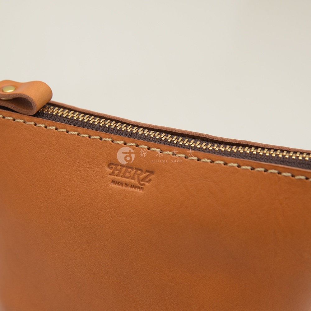 職人手作皮革三角收納包，以鞣製皮革製成，設有金色拉鍊與車縫細節，壓印有「HERZ」品牌標誌與「MADE IN JAPAN」字樣。