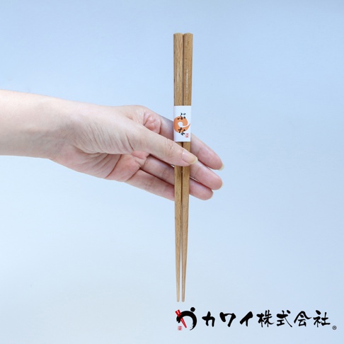 手持一雙天然原色木筷，筷身上繫有印有橘色卡通圖案的白色紙帶。