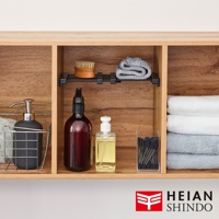 木紋層架上展示著一個黑色按壓瓶皂液器，置於銀色金屬置物籃內；一個深棕色噴霧瓶及一個透明方形瓶裝黃色液體，旁為裝有黑色棉花的透明盒；最右側疊放著白色及淺藍色毛巾。