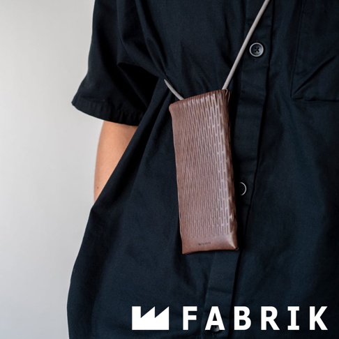 FABRIK 品牌標誌旁的皮革隨形貼合伸縮小包，以精緻的編織皮革紋理，懸掛於身著黑色襯衫的人身上