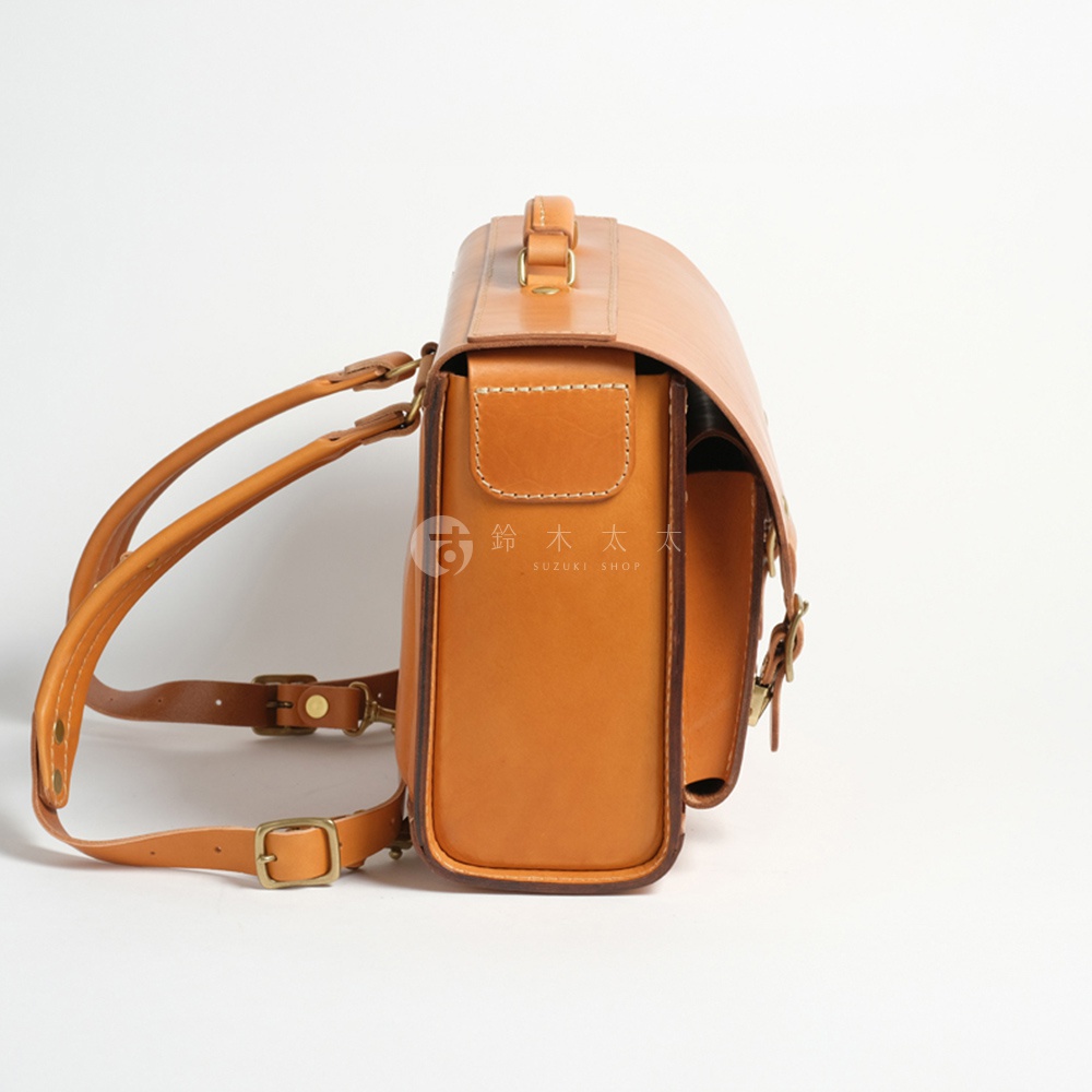 一個棕色皮革製成的橫式背包，從側面拍攝，展示了其精緻的縫線和金屬扣環。