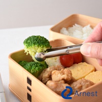 不鏽鋼料理夾夾著綠色花椰菜，置於木質便當盒中，盒內有炸雞塊、番茄和玉子燒。