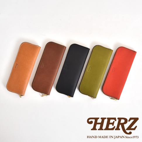 五個不同顏色的皮革筆袋，從左到右分別是淺棕色、深棕色、黑色、橄欖綠色和紅色，皆有拉鍊封口，上面壓印有HERZ字樣。