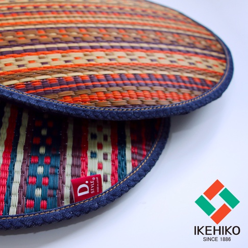 兩個圓形藺草紋織坐墊，一個以棕色、橘色、紫色和米色條紋交織，另一個以紅、藍、綠和米色條紋交織，邊緣皆以牛仔布包邊，並有紅色品牌標籤。