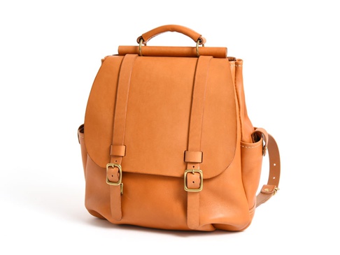 一個棕褐色皮革雙扣後背包，具有頂部提把、可調節肩帶，以及側面口袋。