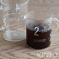 透明玻璃咖啡沖泡壺組，包含一個裝有深色咖啡的帶把手沖泡壺，壺身上印有白色數字「2」和「1」及英文標語，以及一個較大的空量杯，兩個沖泡壺均有白色刻度標記。