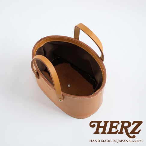 職人手作皮革束口手提包，淺棕色光滑皮革，圓潤提把，內裡為深棕色布料，簡潔的束口設計。