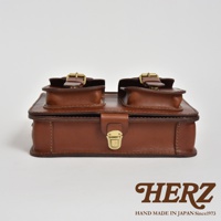 職人手作皮革雙口袋兩用單肩包 A-19，採用咖啡色皮革製作，包身有兩個上方帶有皮帶釦的翻蓋口袋，正面有一個黃銅色金屬鎖扣，整體呈現簡約復古風格。