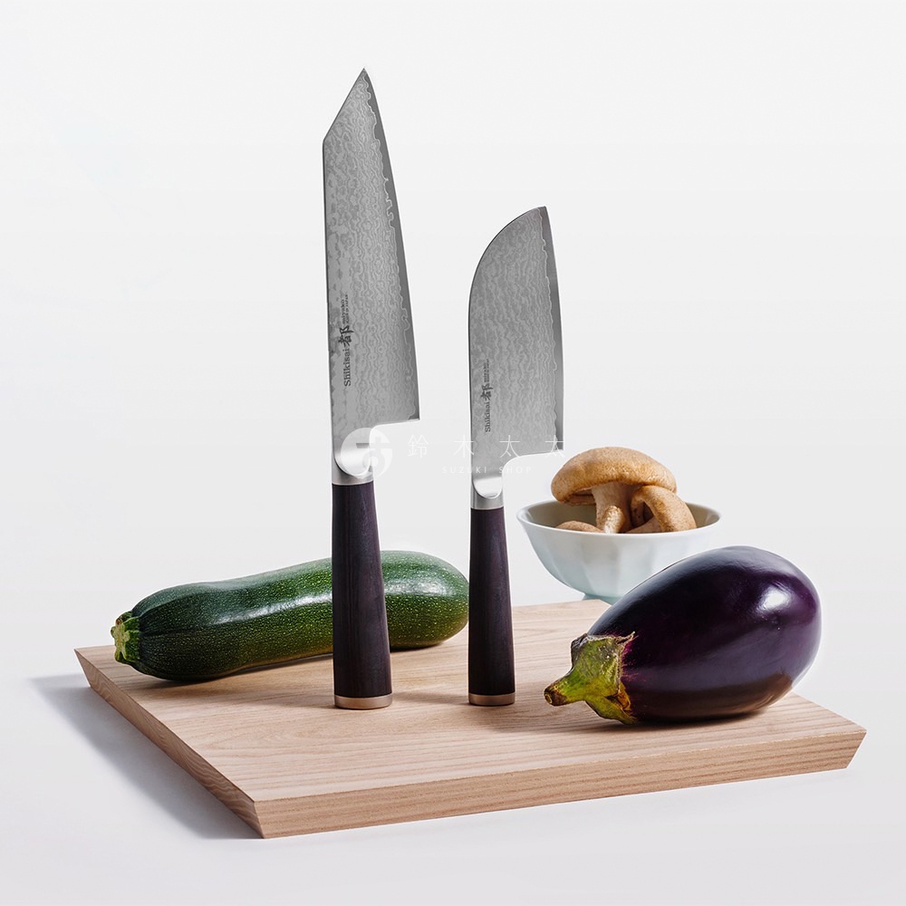 兩把日式廚刀，一把日式菜刀、一把日式三德刀，放在木砧板上，旁邊有一根櫛瓜、一顆茄子和一碗香菇。