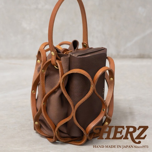 日本Herz手工皮革Organ編織水桶包，展現精緻工藝與獨特設計，深棕色皮革與帆布材質的完美結合，搭配品牌Logo與製造地資訊。