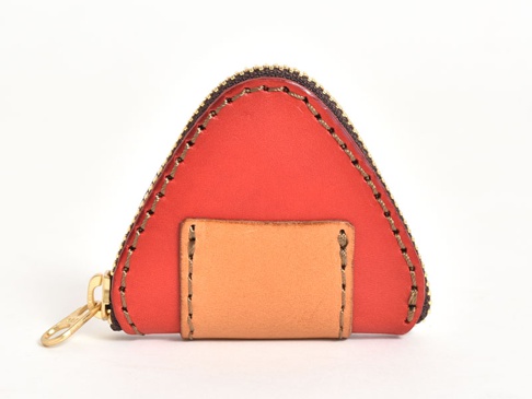 紅色皮革製作的三角飯糰造型零錢包，搭配黃銅拉鍊與兩片淺棕色皮革裝飾，手工縫線明顯。