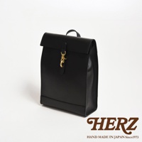 黑色皮革製成，紙袋造型後背包，設有翻蓋開口及金屬扣環，簡約設計，展現職人手作質感。