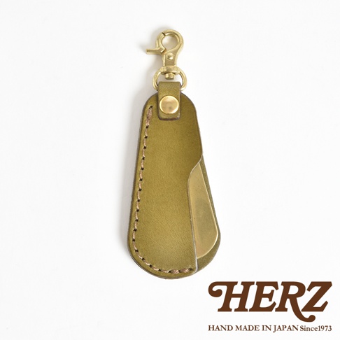 橄欖綠皮革隨身金屬鞋拔，搭配黃銅鑰匙圈，皮革邊緣有縫線細節，設計簡約。