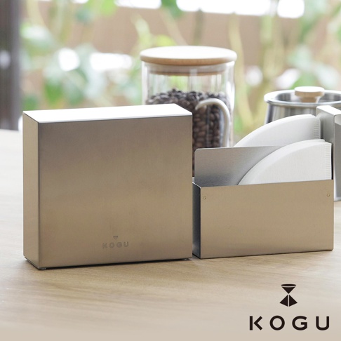 日製 KOGU 珈琲考具分隔式不鏽鋼咖啡濾紙收納盒，搭配玻璃咖啡豆儲存罐與金屬手沖咖啡壺，置於木質桌面。