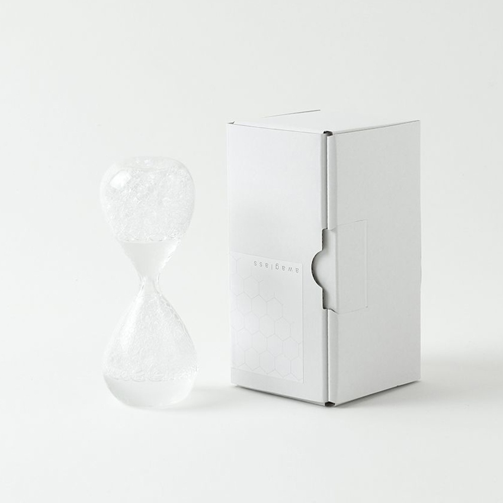 awaglass 泡時計，透明玻璃材質，內部裝有細小氣泡，呈現流動感。旁邊擺放著白色方形產品包裝盒，盒面上印有品牌名稱「awaglass」及蜂巢圖案。
