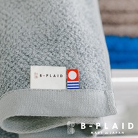 淺灰色毛巾，帶有「B-PLAID」字樣的白色標籤，以及一個紅色、白色和藍色條紋的方形標籤。