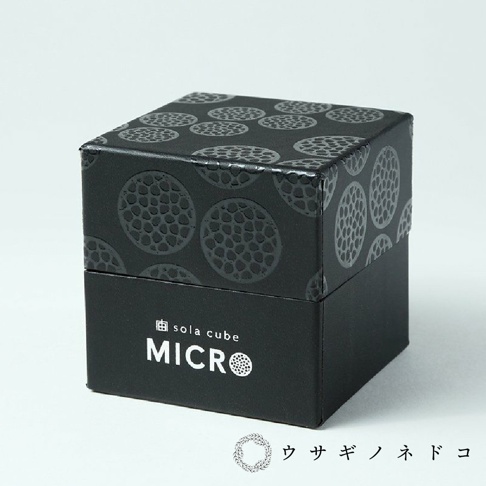 黑色方形紙盒，盒蓋頂部與側面印有重複的灰色圓形圖案，每個圓形內有雷射雕刻的細小網格結構。盒身正面印有白色「sola cube MICRO」字樣。