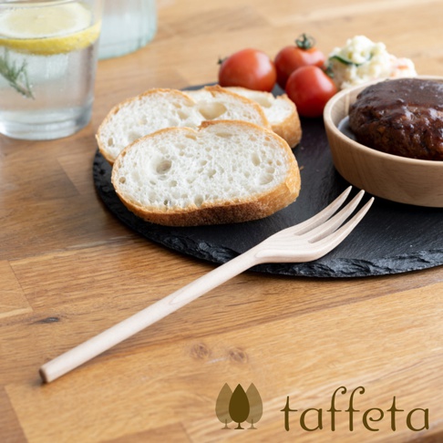 楓木製餐叉，呈現自然淺木色，有三叉設計，放置於木質桌面，背景為餐點與飲料。