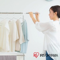 簡約不鏽鋼曬衣架，掛有四件不同顏色的棉麻質地衣物，包括白色、米色、淺棕色和淺藍色。一位女士正調整曬衣架的水平桿。