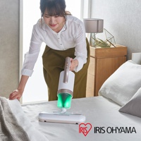 粉色手持式除蹣吸塵器，配備綠色透明集塵筒，白色機身與玫瑰金手把，搭配寬扁的吸頭，正在清潔白色床鋪。