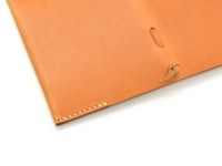 淺棕色皮革製成的書套，帶有縫線細節，一側有皮革繩穿過孔洞並打結。