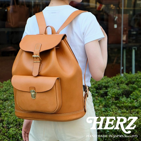 職人手作經典皮革後背包，採用溫暖的淺棕色皮革，設有翻蓋抽繩主袋及前置小口袋，以精緻的縫線點綴，呈現自然質樸的風格。