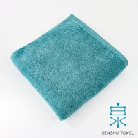 一張藍綠色長纖浴巾，材質蓬鬆柔軟，邊緣有縫線，左上角為浴巾一角，右下角有日文「泉」字樣與 SENSYU TOWEL 商標。