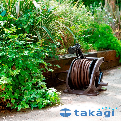 室外灑水組，配備棕色軟管及黑色噴頭，置於深棕色塑膠捲盤架上，架旁有綠色植物及木製圍欄。