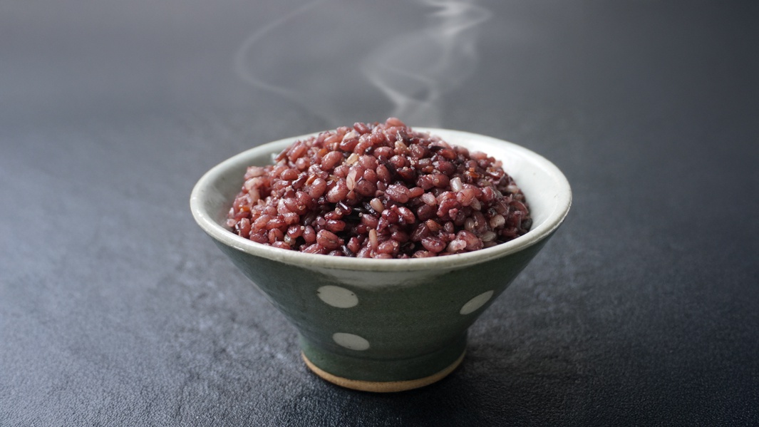 一碗盛滿深紅色十六穀米的陶瓷碗，碗身為深綠色，帶有白色圓點裝飾。