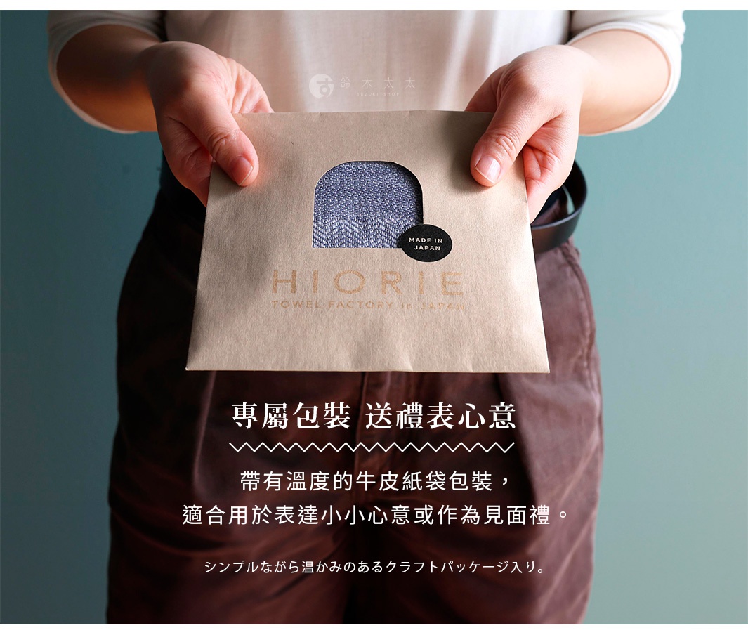 一名女子雙手捧著一個牛皮紙信封，信封開口處露出一個藍色人字紋的方巾，上面有HIORIE品牌字樣和MADE IN JAPAN貼紙。