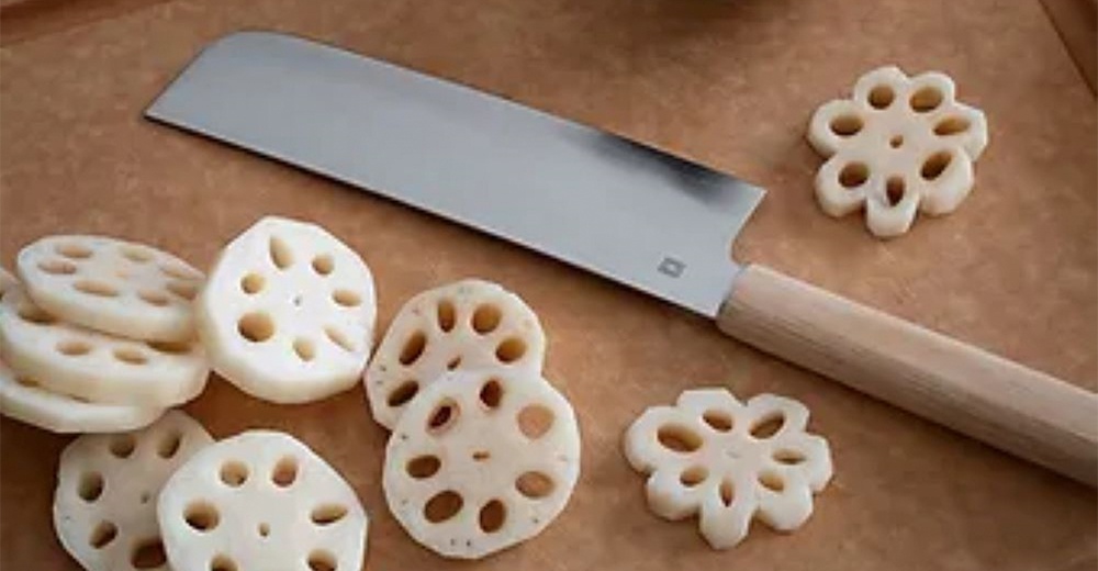 Yuri 菜切刀，刀刃為銀色不鏽鋼材質，配有淺木色刀柄。周圍散落著多片切成圓形且帶有孔洞的蓮藕片。