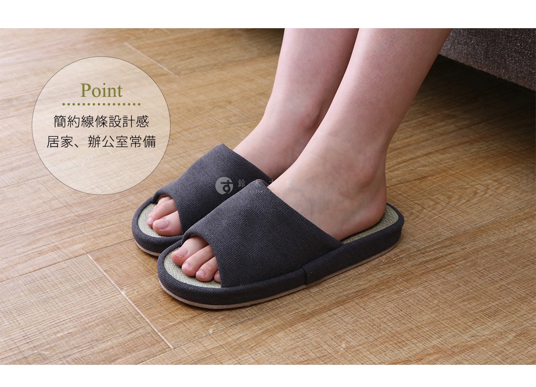 一雙深灰色藺草透氣室內拖鞋，鞋面為織布材質，鞋底內襯為藺草編織，露出腳趾，穿著於木質地板上。