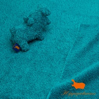 藍綠色竹棉混紡布料上，有一個藍色標籤的淺藍色河馬造型抓握玩偶，玩偶材質柔軟，布料表面有絨毛感，右下角有橘色河馬圖案及品牌Logo。