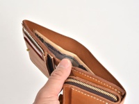 職人手作皮革直式卡片收納雙折短夾，原色皮革材質，內含日圓紙鈔及信用卡，以精緻縫線製作，展現皮革質感。