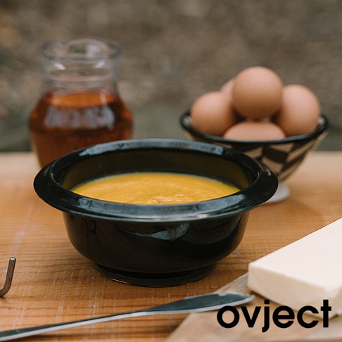 黑色琺瑯湯鍋盛有黃色濃湯，旁有雞蛋、奶油與玻璃壺。