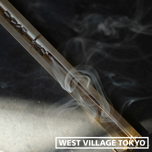 黃銅夾式水平線香架，線香燃燒中，散發白色煙霧，整體呈金屬光澤，置於深色背景上。