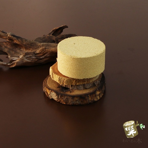 圓柱狀的淡黃色撫味塊，堆疊在兩個不同尺寸的木紋圓形底座上，背景左側為一塊乾燥的深褐色樹枝。