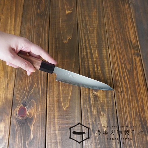 手持一把Chromax鋼水果刀，刀刃呈銀色，帶有波浪紋路。刀柄為胡桃木材質，末端為黑色。刀身下方是木紋桌面，右下角有「BABA CUTLERY WORKS SAKAI JAPAN 1916」的文字標誌。